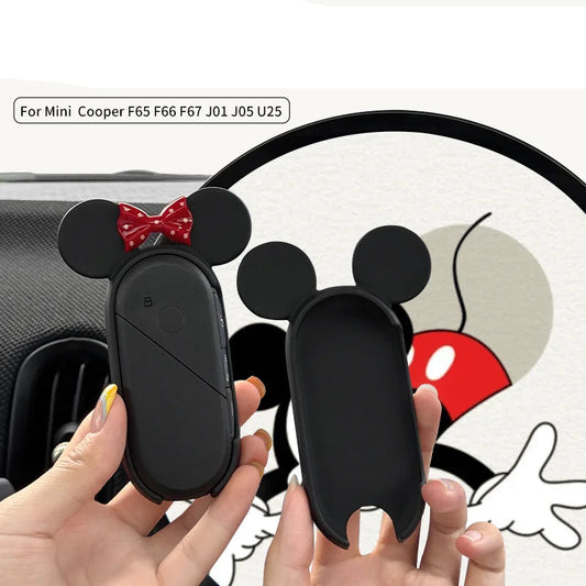 Black key case with red bow and white face design held by hands, with cartoon illustration in the background.